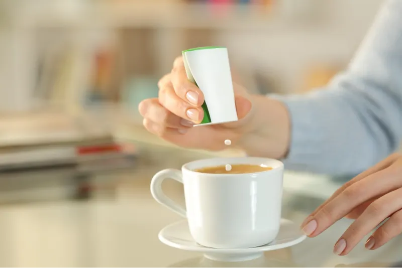 Donna che mette delle pastiglie di edulcoranti naturali sintetici nel cappuccino