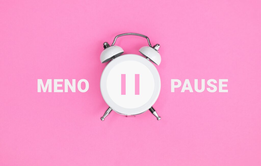 Una sveglia con all'interno il simbolo di "pausa". Lo sfondo è rosa e c'è la scritta "Menopause"